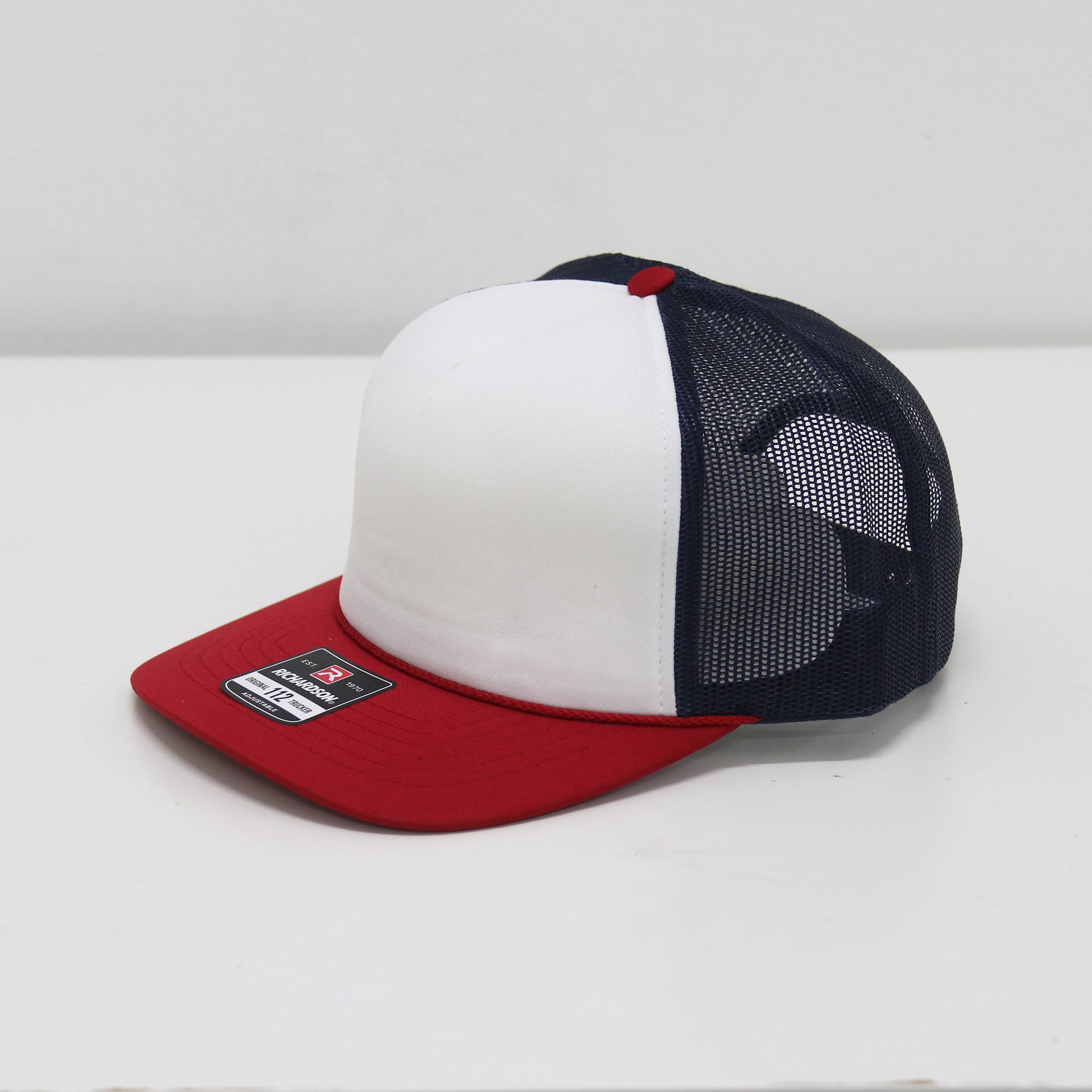 Trucker hat with white front panel, red bill, and navy mesh back on a white background